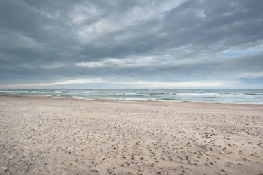 Kumlu bir sahilden (kum tepeleri) Baltık denizinin panoramik görüntüsü. Parlayan bulutlar, dalgalar ve su sıçramalarıyla dramatik bir gökyüzü. Idyllic deniz manzarası. Sıcak kış havası, iklim değişikliği, doğa. Danimarka