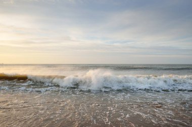 Gün batımında Baltık kıyıları (kum tepeleri). Yumuşak güneş ışığı, parlayan bulutlar, dalgalar ve su fışkıran berrak gökyüzü. Idyllic deniz manzarası. Liepaja, Letonya, Avrupa. Sıcak kış havası, iklim değişikliği, doğa