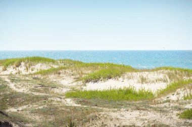 Güneşli bir günde Baltık kıyılarının panoramik manzarası. Açık mavi gökyüzü, kum tepeleri, kum tepeleri, turkuaz su. Yaz manzarası. Doğa, ekoloji. Eko-turizm, yürüyüş. Eğlence, yerel seyahat.
