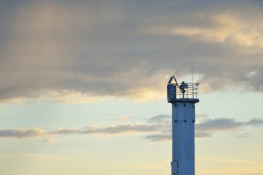 Güneş pilli deniz feneri. Baltık Denizi. Fırtınadan sonra dramatik günbatımı gökyüzü. Parlayan bulutlar, altın güneş ışığı. Umut ve barışın sembolü. Mimarlık, seyahat yerleri, navigasyon, yelkencilik.