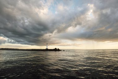 Güneş pilli deniz feneri. Baltık Denizi. Fırtınadan sonra dramatik günbatımı gökyüzü. Parlayan bulutlar, altın güneş ışığı. Umut ve barışın sembolü. Mimarlık, seyahat yerleri, navigasyon, yelkencilik.