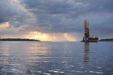 Fırtınadan sonra Baltık Denizi. Kargo gemisi iskele terminaline yükleniyor, vinçler yaklaşıyor. Dramatik gün batımı gökyüzü. Nakliye, lojistik, küresel iletişim, endüstri, çevre