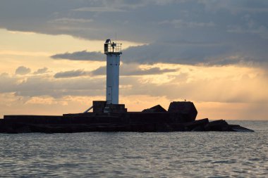 Güneş pilli deniz feneri. Baltık Denizi. Fırtınadan sonra dramatik günbatımı gökyüzü. Parlayan bulutlar, altın güneş ışığı. Umut ve barışın sembolü. Mimarlık, seyahat yerleri, navigasyon, yelkencilik.