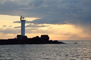 Güneş pilli deniz feneri. Baltık Denizi. Fırtınadan sonra dramatik günbatımı gökyüzü. Parlayan bulutlar, altın güneş ışığı. Umut ve barışın sembolü. Mimarlık, seyahat yerleri, navigasyon, yelkencilik.