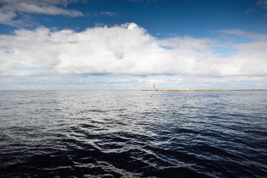 Gün batımında Baltık Denizi. Fırtınadan sonra dramatik mavi gökyüzü, süslemeli kümülüs bulutları. Arka planda deniz feneri var. Destansı bulut manzarası. Doğa, çevre, ekoloji, meteoroloji, kasırga, kararsız hava