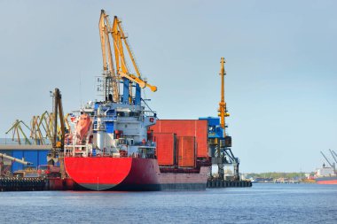 Liman terminalinde büyük bir kargo gemisi yükleniyor, arka planda vinçler var. Yük taşımacılığı, lojistik, küresel iletişim, ekonomi, ticaret, sanayi, özel ekipman