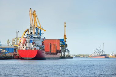 Liman terminalinde büyük bir kargo gemisi yükleniyor, arka planda vinçler var. Yük taşımacılığı, lojistik, küresel iletişim, ekonomi, ticaret, sanayi, özel ekipman