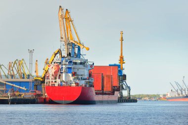 Liman terminalinde büyük bir kargo gemisi yükleniyor, arka planda vinçler var. Yük taşımacılığı, lojistik, küresel iletişim, ekonomi, ticaret, sanayi, özel ekipman
