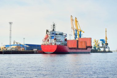 Liman terminalinde büyük bir kargo gemisi yükleniyor, arka planda vinçler var. Yük taşımacılığı, lojistik, küresel iletişim, ekonomi, ticaret, sanayi, özel ekipman