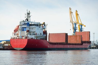 Liman terminalinde büyük bir kargo gemisi yükleniyor, arka planda vinçler var. Yük taşımacılığı, lojistik, küresel iletişim, ekonomi, ticaret, sanayi, özel ekipman