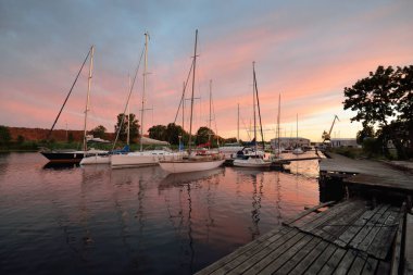 Günbatımında yat limanında demirlemiş zarif ve modern yelkenliler. Dramatik gökyüzü, parlayan altın bulutlar. Tatiller, ulaşım, spor, eğlence, turizm, seyahat, liman