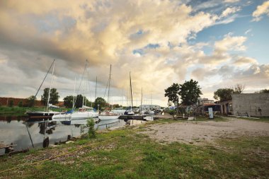 Günbatımında yat limanında demirlemiş zarif ve modern yelkenliler. Dramatik gökyüzü, parlayan altın bulutlar. Tatiller, ulaşım, spor, eğlence, turizm, seyahat, liman