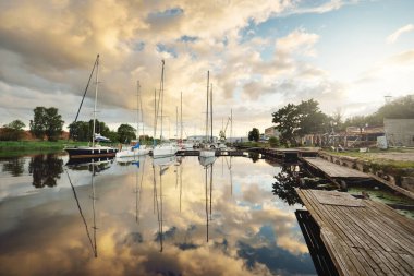 Günbatımında yat limanında demirlemiş zarif ve modern yelkenliler. Dramatik gökyüzü, parlayan altın bulutlar. Tatiller, ulaşım, spor, eğlence, turizm, seyahat, liman