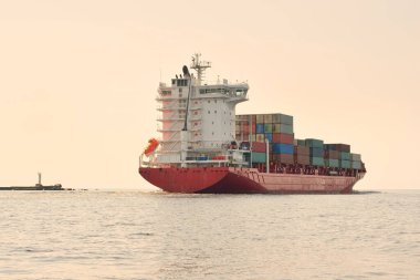 Konteyner gemisi (168 metre uzunluğunda) gün batımında limandan ayrılıyor. Baltık Denizi. Yük taşımacılığı, lojistik, küresel iletişim, dünya çapında taşımacılık, ekonomi, iş dünyası, sanayi