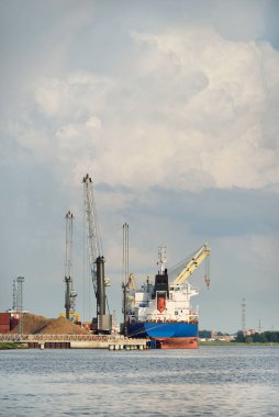 Büyük kargo gemisi (toplu taşıyıcı, 187 metre uzunluğunda) iskele terminalinde yükleme, arka planda vinçler. Yük taşımacılığı, lojistik, küresel iletişim, ekonomi, ticaret, sanayi