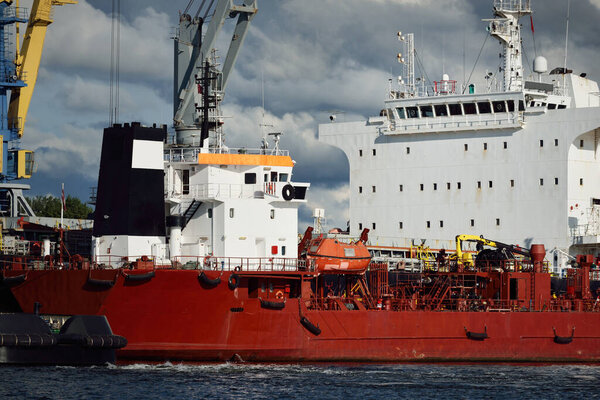 Грузовые суда загружаются в портовый терминал. Краны на заднем плане. Балтийское море. Бункеровка, производство топлива и электроэнергии, снабжение, технологии, логистика, услуги, промышленность, бизнес, торговля