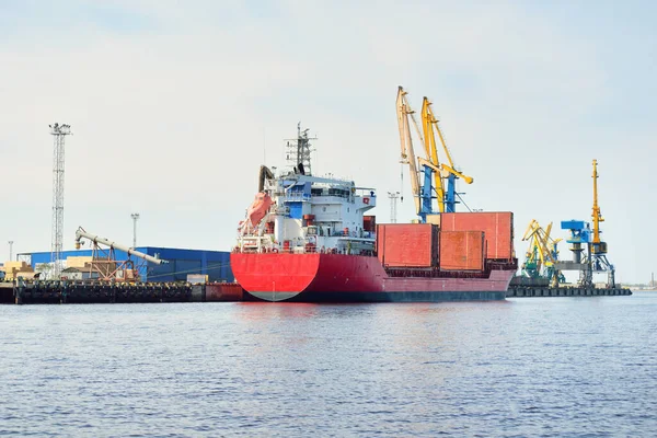 Liman terminalinde büyük bir kargo gemisi yükleniyor, arka planda vinçler var. Yük taşımacılığı, lojistik, küresel iletişim, ekonomi, ticaret, sanayi, özel ekipman