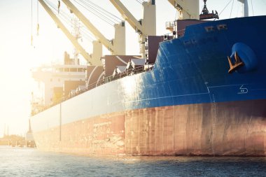 Liman terminalinde büyük bir kargo gemisi yükleniyor, arka planda vinçler var. Yük taşımacılığı, deniz taşımacılığı, lojistik, küresel iletişim, dünya çapında taşımacılık, ekonomi, ticaret, sanayi