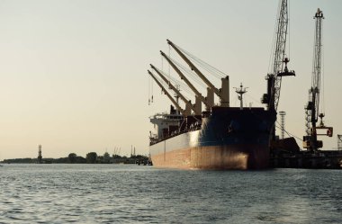 Büyük kargo gemisi (toplu taşıyıcı, 187 metre uzunluğunda) iskele terminalinde yükleme, arka planda vinçler. Yük taşımacılığı, lojistik, küresel iletişim, ekonomi, ticaret, sanayi