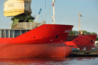 Kırmızı gemi (genel kargo, 89 metre uzunluğunda) iskele terminalinde yükleme, arka planda vinç. Yük taşımacılığı, lojistik, küresel iletişim, dünya çapında taşımacılık, ekonomi, iş dünyası, sanayi