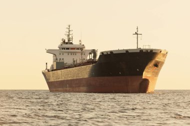 Büyük bir kargo gemisi (kimyasal tanker, 184 metre uzunluğunda) gün batımında açık denizde yol alır. Altın güneş ışığı. Yük taşımacılığı, yakıt, enerji üretimi, denizcilik gemisi, lojistik, ekonomi, sanayi