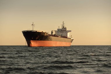 Büyük bir kargo gemisi (kimyasal tanker, 184 metre uzunluğunda) gün batımında açık denizde yol alır. Altın güneş ışığı. Yük taşımacılığı, yakıt, enerji üretimi, denizcilik gemisi, lojistik, ekonomi, sanayi