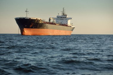 Büyük bir kargo gemisi (kimyasal tanker, 184 metre uzunluğunda) gün batımında açık denizde yol alır. Altın güneş ışığı. Yük taşımacılığı, yakıt, enerji üretimi, denizcilik gemisi, lojistik, ekonomi, sanayi