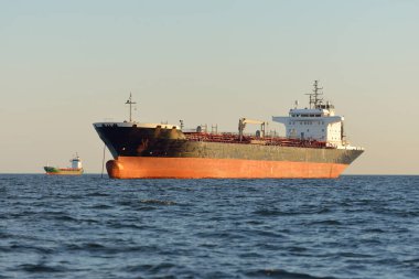 Büyük bir kargo gemisi (kimyasal tanker, 184 metre uzunluğunda) gün batımında açık denizde yol alır. Altın güneş ışığı. Yük taşımacılığı, yakıt, enerji üretimi, denizcilik gemisi, lojistik, ekonomi, sanayi