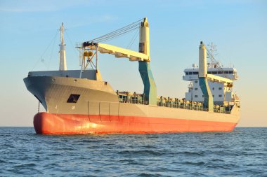 Büyük vinç gemisi (genel yük, 146 metre uzunluğunda) gün batımında açık denizde yol alır. Altın güneş ışığı. Yük taşımacılığı, lojistik, küresel iletişim, ekonomi, sanayi, dünya çapında taşımacılık