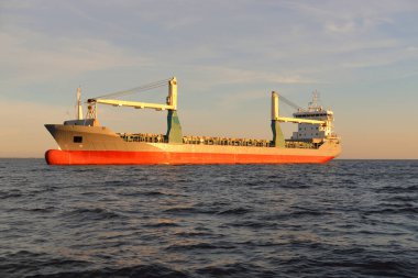 Büyük vinç gemisi (genel yük, 146 metre uzunluğunda) gün batımında açık denizde yol alır. Altın güneş ışığı. Yük taşımacılığı, lojistik, küresel iletişim, ekonomi, sanayi, dünya çapında taşımacılık