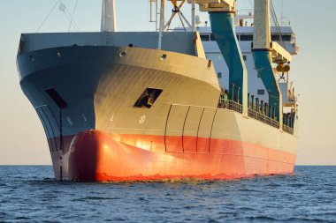 Gün batımında açık denizde yelken açan büyük bir yük vinci gemisi. Altın güneş ışığı. Yük taşımacılığı, deniz taşımacılığı, lojistik, küresel iletişim, ekonomi, iş dünyası, sanayi, dünya çapında nakliye