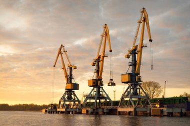 Riga, Letonya 'daki modern kargo limanı terminali. Vinçler yakın plan. Dramatik bir gökyüzü. Baltık Denizi. Yük taşımacılığı, lojistik, küresel iletişim, ekonomi, ticaret, sanayi, arz, özel ekipman