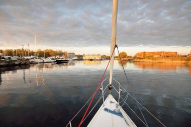 Beyaz yat gün batımında limana varacak. Güverteden pruva ve yelkenlere kadar yakın çekim. Fırtınadan sonra dramatik bir gökyüzü. Baltık Denizi. Deniz aracı, ulaşım, hizmet, spor, eğlence kavramları