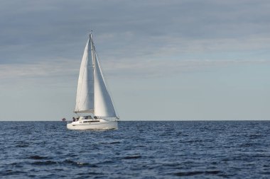 Baltık Denizi 'nde yelkenli bir yat. Gün batımı. Fırtınadan sonra dramatik bir gökyüzü, yumuşak güneş ışığı. Ulaşım, seyahat, seyahat, yat yarışı, spor, eğlence, eğlence, eğlence, yaşam tarzı, aile.