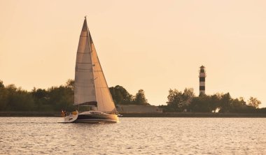 Baltık Denizi 'nde yelkenli bir yat. Deniz fenerine yakın çekim. Fırtınadan sonra gün batımı gökyüzü açık. Ulaşım, seyahat, gezi, spor, eğlence, boş zaman aktivitesi, yarış, yelkenli yarışı
