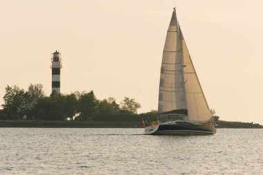 Baltık Denizi 'nde yelkenli bir yat. Deniz fenerine yakın çekim. Fırtınadan sonra gün batımı gökyüzü açık. Ulaşım, seyahat, gezi, spor, eğlence, boş zaman aktivitesi, yarış, yelkenli yarışı