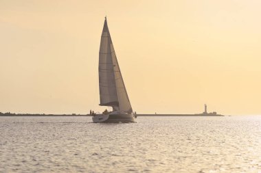 Baltık Denizi 'nde yelkenli bir yat. Deniz fenerine yakın çekim. Fırtınadan sonra gün batımı gökyüzü açık. Ulaşım, seyahat, gezi, spor, eğlence, boş zaman aktivitesi, yarış, yelkenli yarışı