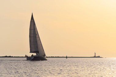 Baltık Denizi 'nde yelkenli bir yat. Deniz fenerine yakın çekim. Fırtınadan sonra gün batımı gökyüzü açık. Ulaşım, seyahat, gezi, spor, eğlence, boş zaman aktivitesi, yarış, yelkenli yarışı