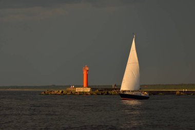 Baltık Denizi 'nde yelkenli bir yat. Gün batımı. Fırtınadan sonra dramatik bir gökyüzü, yumuşak güneş ışığı. Ulaşım, seyahat, seyahat, yat yarışı, spor, eğlence, eğlence, eğlence, yaşam tarzı, aile.