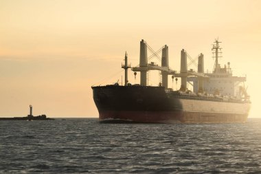 Büyük bir kargo gemisi (179.99 metre uzunluğunda) gün batımında Baltık Denizi 'nde yol alır. Nakliye, lojistik, küresel iletişim, ekonomi, sanayi, arz, çevre