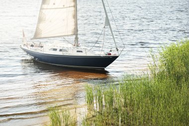 Kumlu kıyıya demirli mavi şalopeli yat (kumsalda otlarla kaplanmış). İsveç 'te, Avrupa' da. Doğa, yaz tatilleri, eğlence, gezi, spor, ulaşım. Hava görünümü