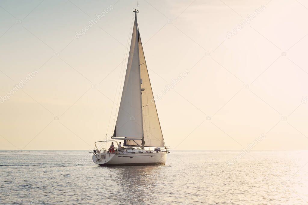 White sloop rigged yacht sailing in the Baltic sea at sunset. Clear sky after the storm, golden sunlight. Transportation, travel, cruise, sport, recreation, leisure activity, racing, regatta