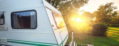 Karavan, gün batımında ağaçların altındaki yeşil çimlere park etmiş. Brittany, Fransa. Tatiller, boş zaman aktiviteleri, eğlence, turizm, yol gezisi, seyahat yerleri, yaşam tarzı