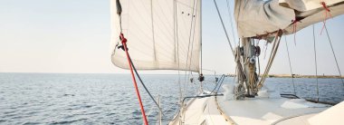 Açık bir günde açık denizde yelken açan beyaz yelkenli bir yat. Güverteden pruvaya bir manzara, direk, yelkenler. Ulaşım, seyahat, gezi, spor, eğlence, boş zaman aktivitesi, yarış, yelkenli yarışı