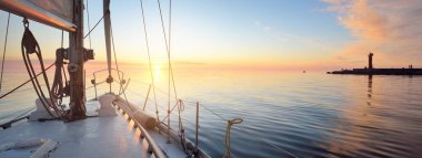 Günbatımında yağmurdan sonra beyaz yat denize açılacak. Güverteden pruvaya kadar yakın çekim. Durgun bir suya yansıyan parlak bulutlarla dolu berrak mavi bir gökyüzü. Idyllic deniz manzarası. Deniz, seyahat, seyahat yerleri