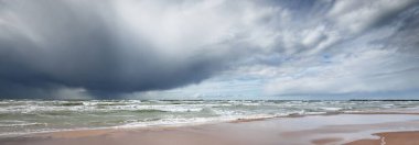 Fırtına sonrası dramatik bulutların altında Baltık Denizi 'nin kumlu sahili. Letonya 'da sızıntı var. Destansı deniz manzarası. Kasırga, fırtına, sert hava, meteoroloji, iklim değişikliği, doğal fenomen
