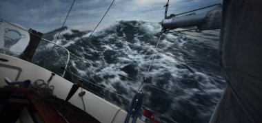 Fırtınada denizde yüzen topuklu bir yat, kokpitten bir manzara. Karanlık dalgalar, su sıçramaları. Uzun pozlama, hareket. Kötü hava, kasırga, tehlike, destansı deniz manzarası. Yarış, yarış, spor