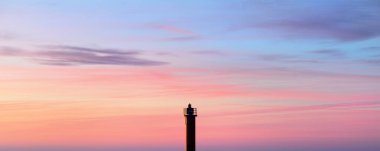 Gün batımında parlak pembe sirrus ve kümülüs bulutlarıyla açık mavi gökyüzü. Güneş pilli deniz feneri. Dramatik bulut manzarası. Resimli panoramik manzara. Navigasyon, sembol: Umut ve barış