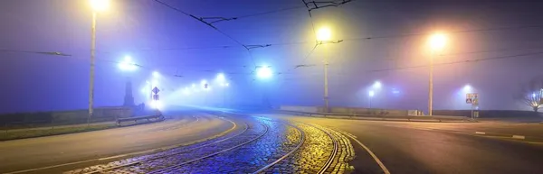 夜には濃い霧の中で照明された空の石の橋を介して路面電車やアスファルトの道路 高速道路 提灯を閉じます ラトビアのリガのドーヴァ川 コンセプトイメージ ネオンカラー — ストック写真