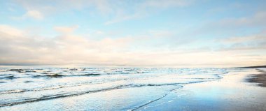 Gün batımında karla kaplı Baltık deniz kıyısından bir manzara. Riga Körfezi, Letonya. Dramatik bir gökyüzü. Kristal berrak mavi su. Kararsız hava, dalgalar ve su sıçramaları. Kış turizmi, küresel ısınma teması